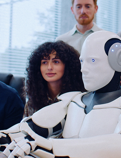 Eine Gruppe von Menschen betrachtet interessiert einen humanoiden Roboter, der vor einem Computer sitzt.